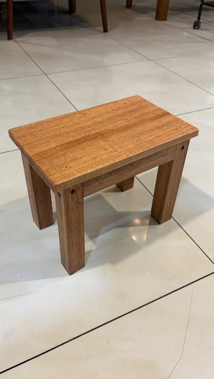 Small rectangular wooden stool with thick legs on a white tiled floor