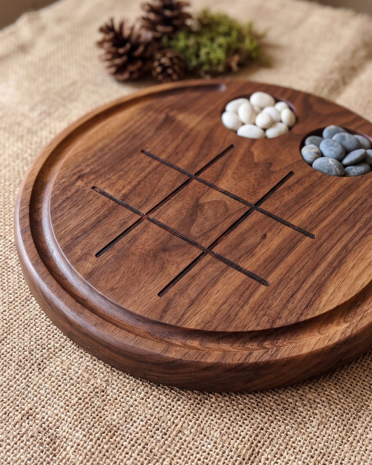 Wooden tic-tac-toe game board with carved grid and smooth stone playing pieces.