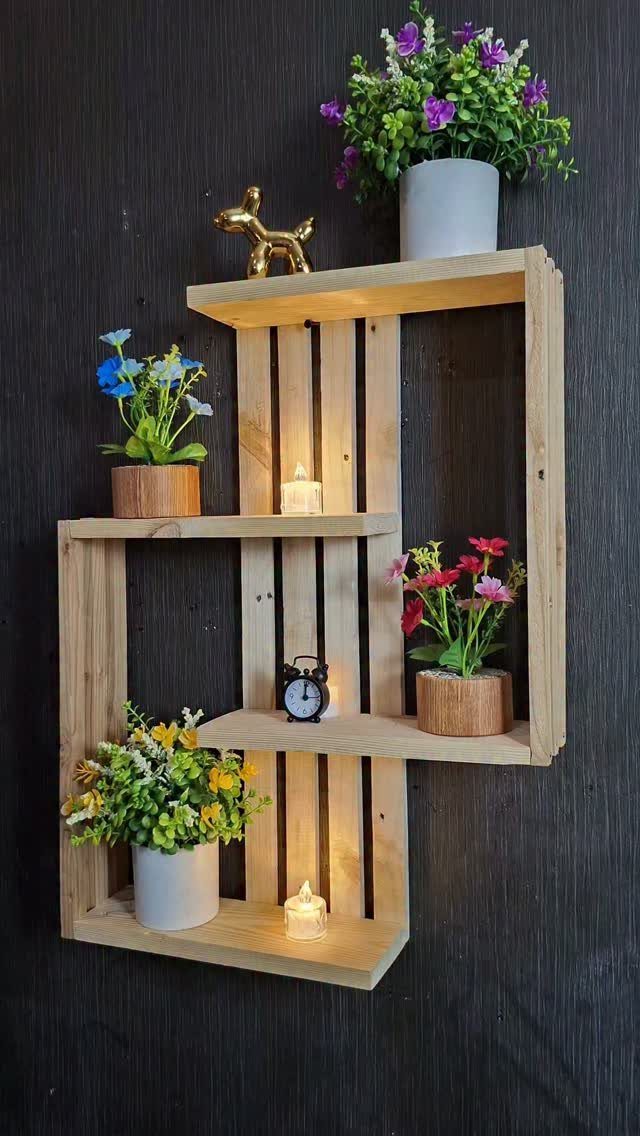 Wooden wall shelf with tiered levels holding plants, candles, and a small clock.
