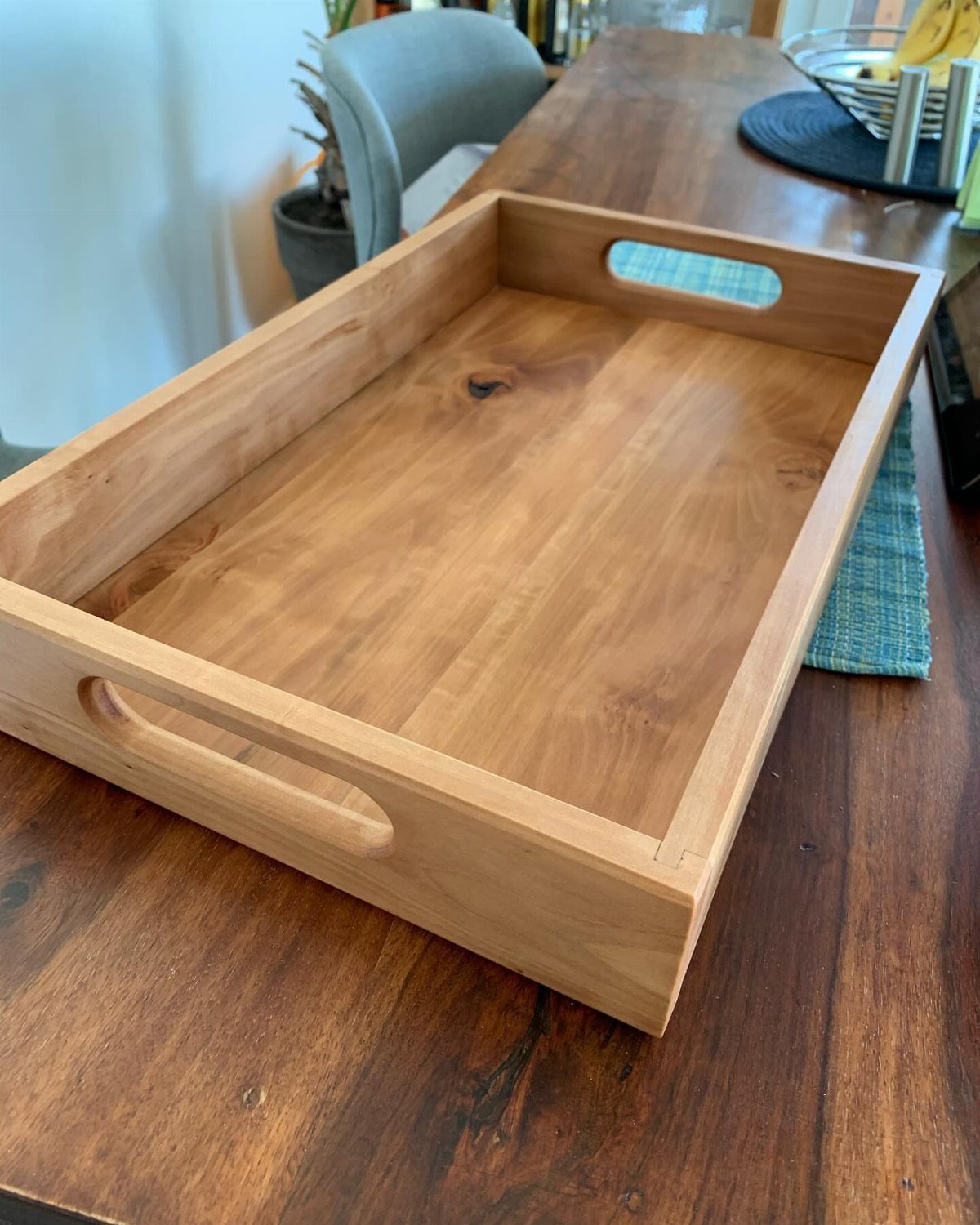 Wooden serving tray with handle cutouts sitting on a dark wood table