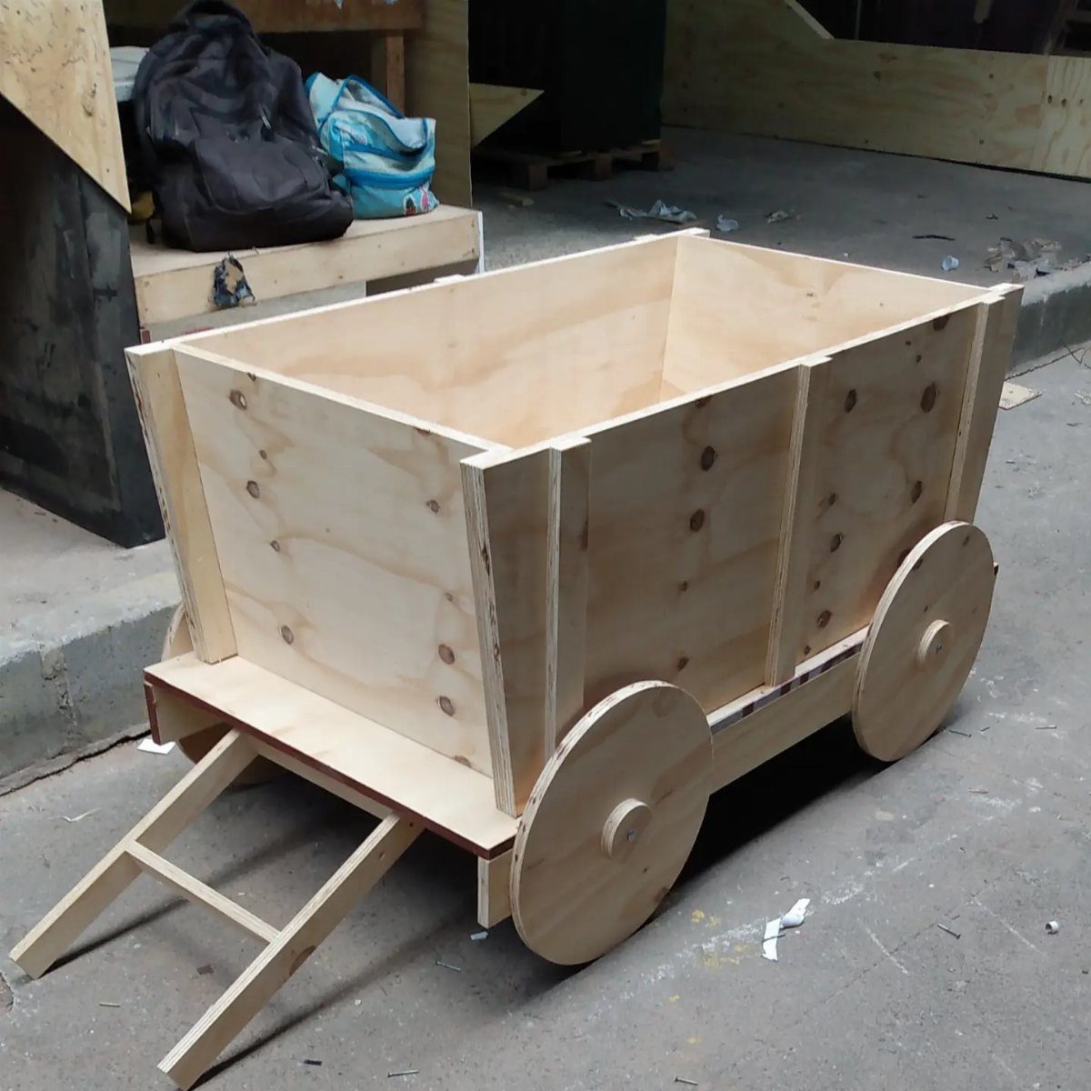 Wooden toy wagon made of light plywood with circular wheels and a handle.