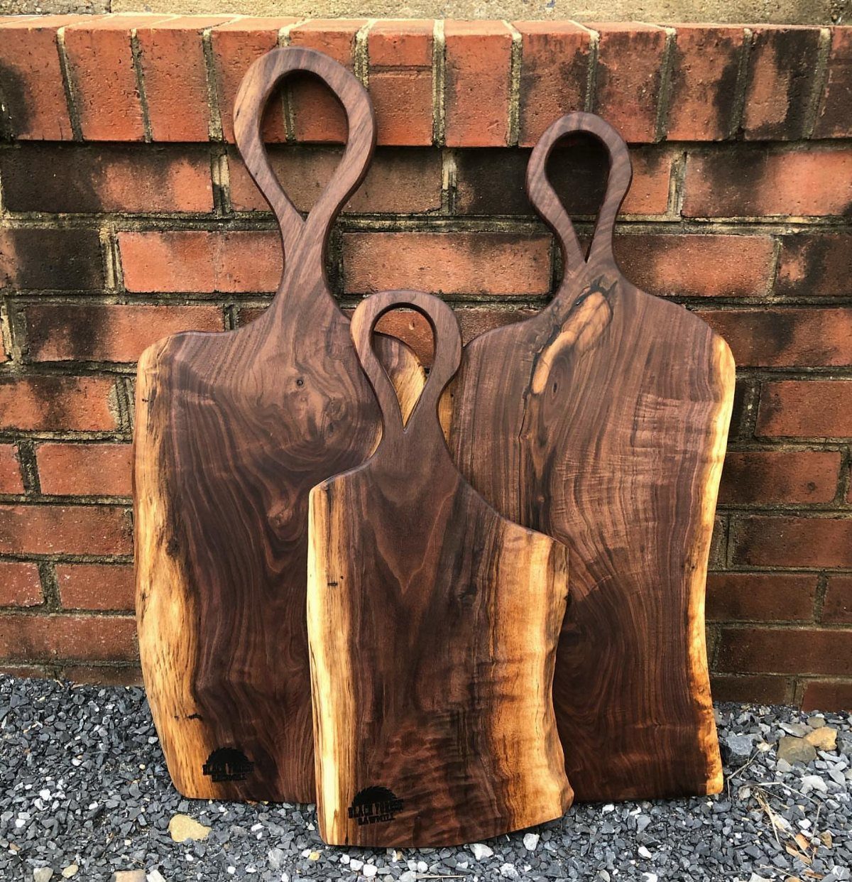 12 Woodworking Ideas to Make Money With Simple Builds 4 Three dark walnut charcuterie boards with handles leaning against a red brick wall.