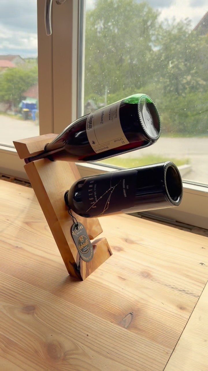 12 Woodworking Ideas to Make Money With Simple Builds 9 Wooden wine rack holding two bottles of wine on a light wood surface.