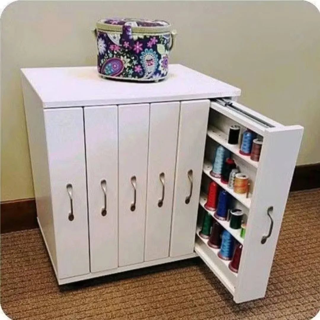 White wooden storage cabinet with a pull-out shelf holding colorful sewing thread spools