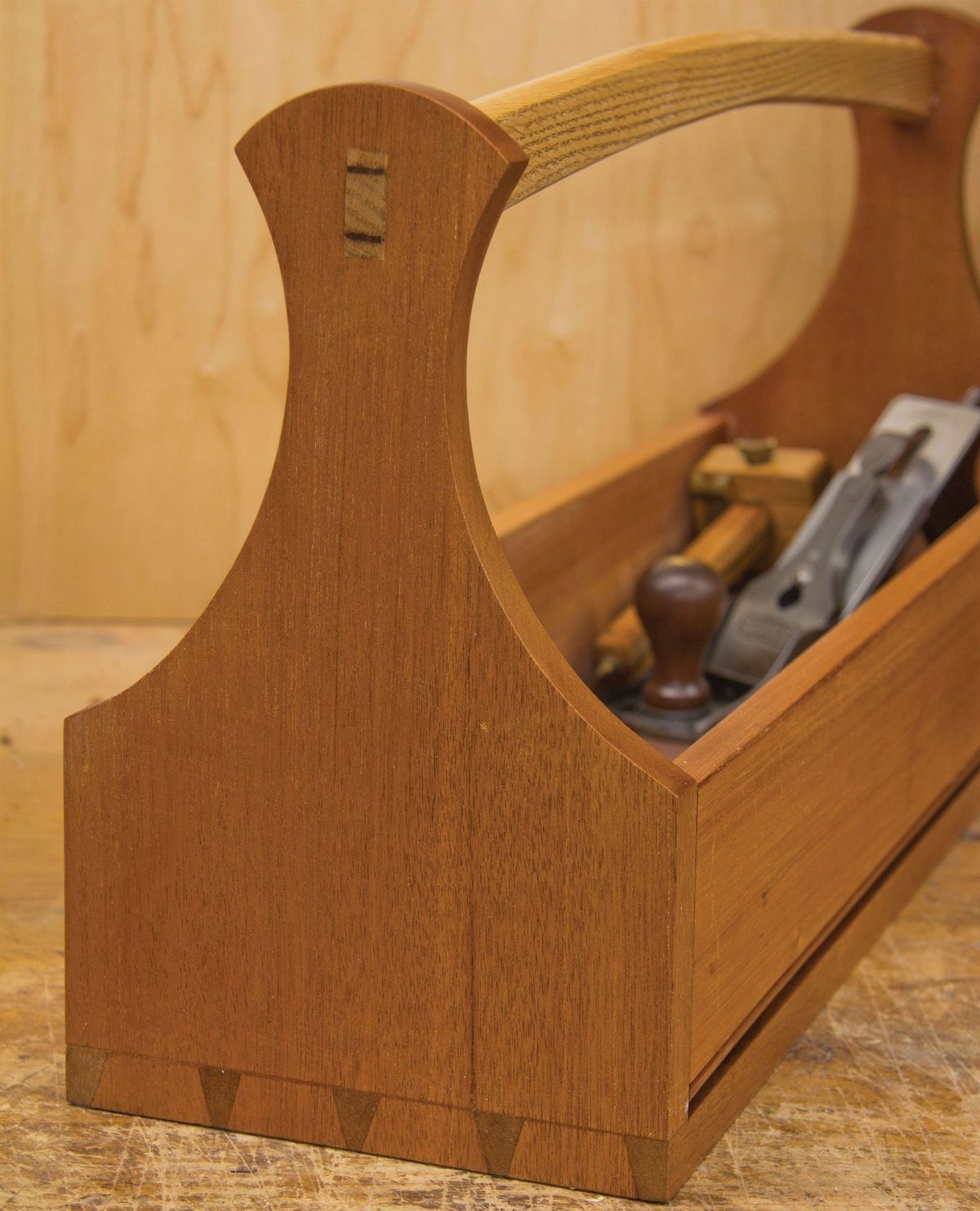 Wooden tool caddy with hand tools resting on a light wood workbench