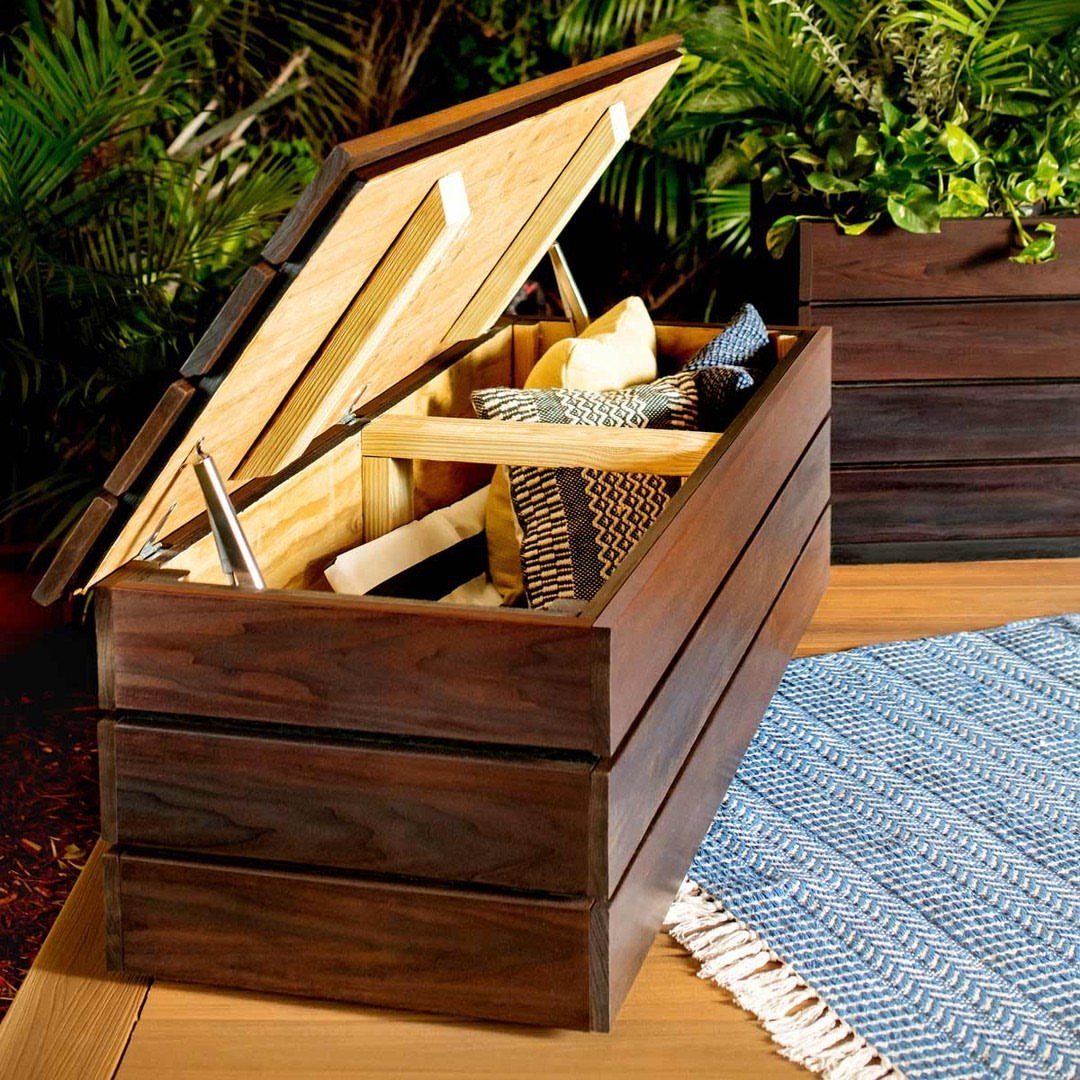 Dark brown wooden storage bench with open lid containing pillows on a deck