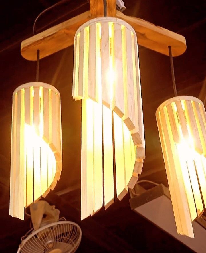 Three wooden slat pendant lights glowing with warm light hanging from a beam.