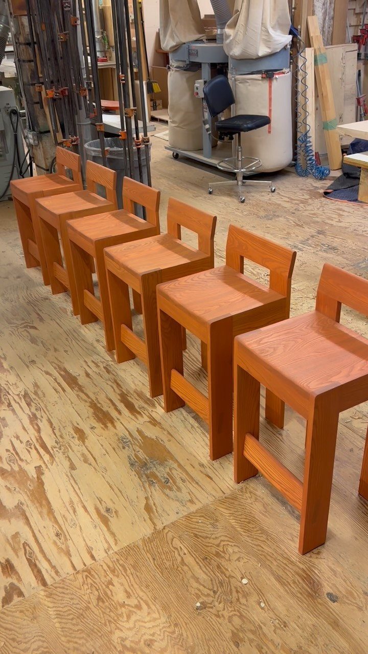 Woodworking Shop Furniture: 4 Ideas for Your Workspace 4 Wooden stools with backrests lined up on a plywood floor in a workshop.