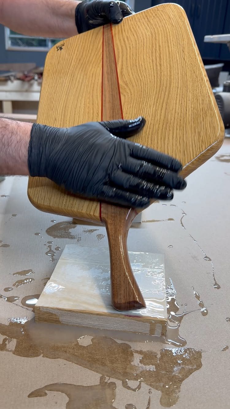 14 Woodworking Shop Projects for Every Skill Level 14 Wooden pizza peel with a red stripe held by gloved hands on a workbench.