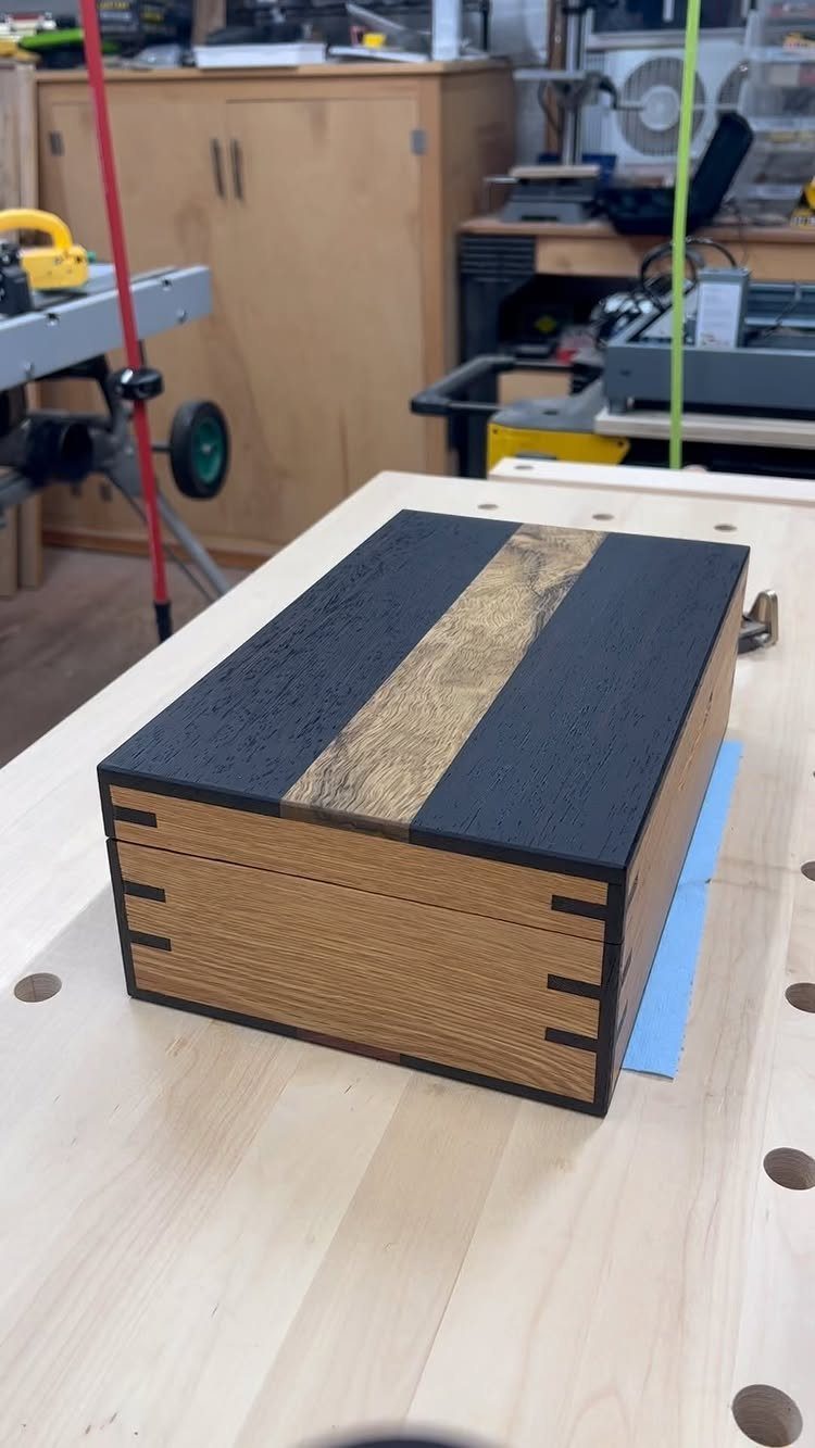 14 Woodworking Shop Projects for Every Skill Level 13 Small wooden jewelry box with black and natural wood stripes on a workbench.