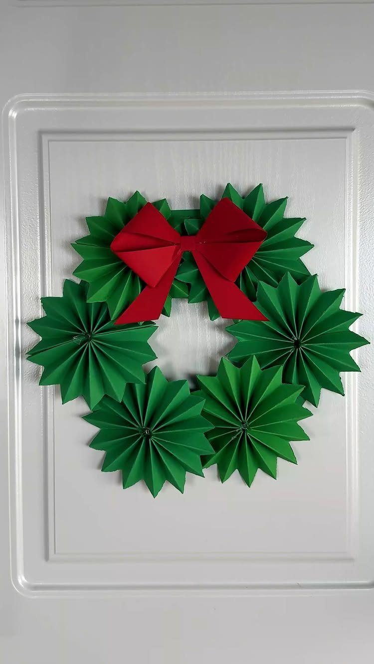 Green pleated paper star wreath with a red bow on a white door.