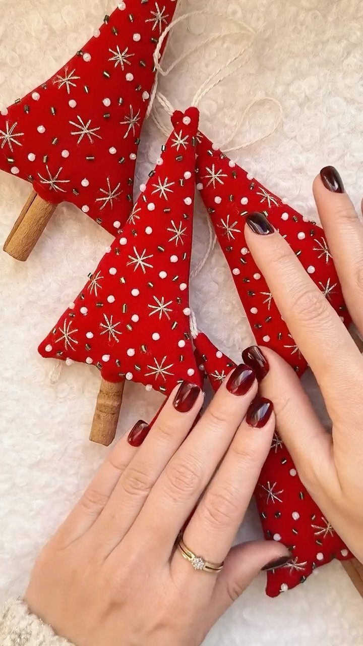Red fabric Christmas tree ornaments with wooden bases held by manicured hands.