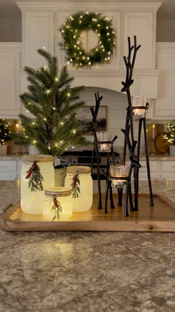 Frosted mason jars and branch candle holders on a wooden tray with a Christmas tree.