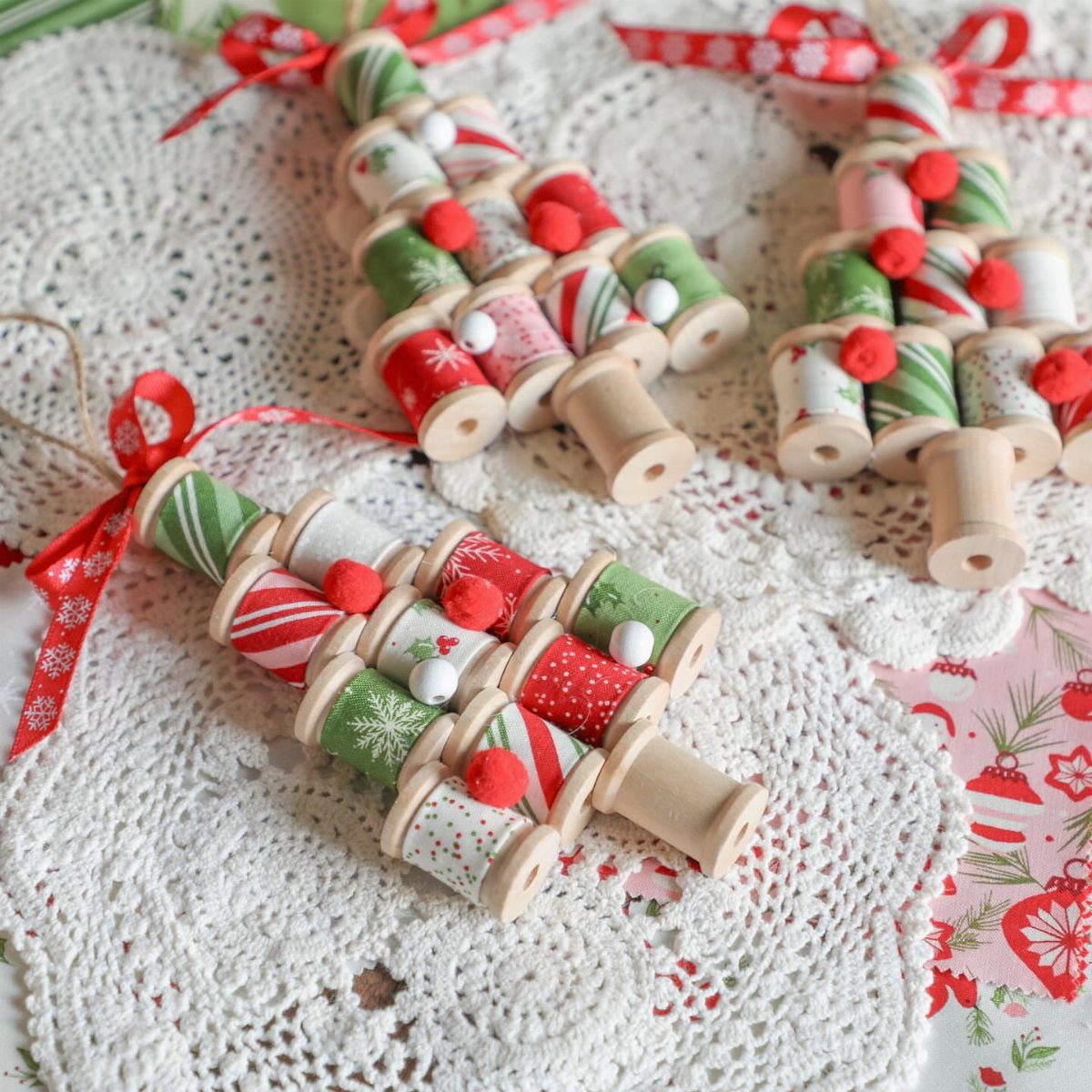 Wooden thread spool Christmas tree ornaments wrapped in festive red and green yarn.