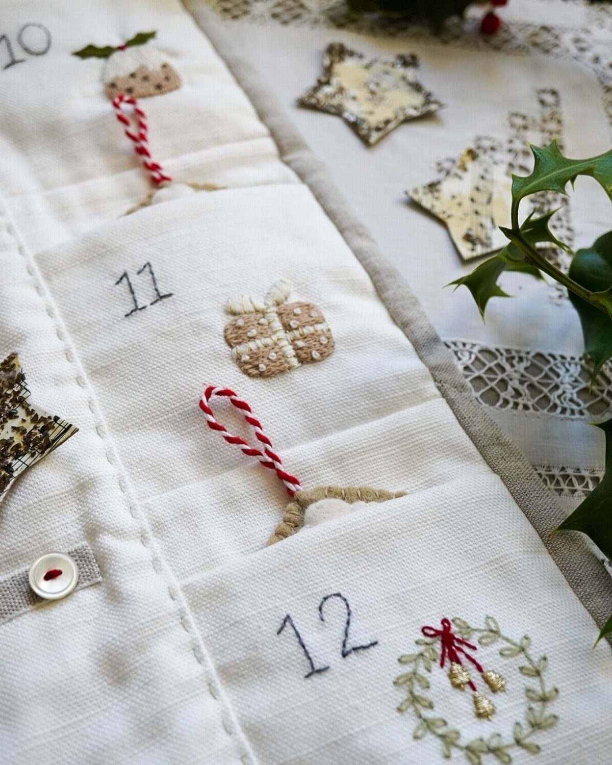 White fabric advent calendar with numbered pockets and hand-stitched Christmas embroidery.