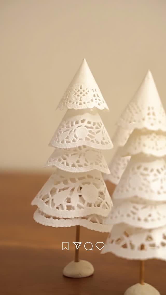 White paper doily Christmas trees standing on small wooden dowels on a brown surface.